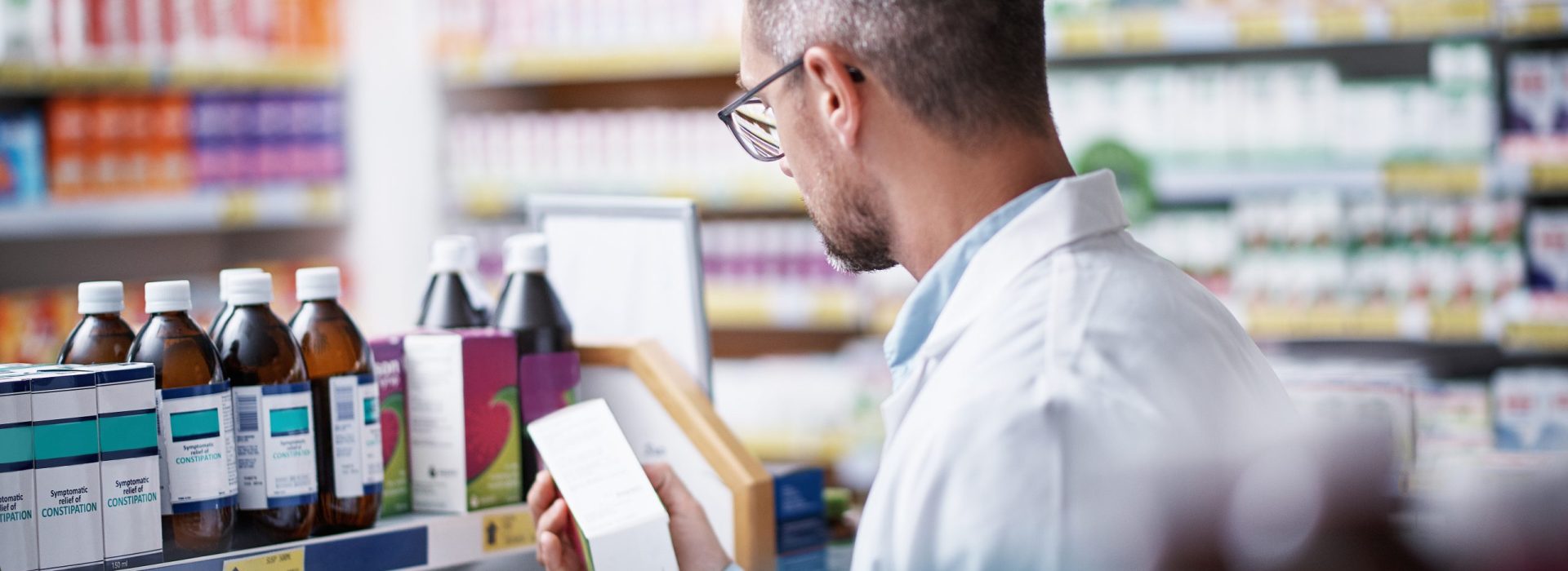 Pharmacist, man and box inspection with clipboard in store for inventory, expiry date or medical info. Chemist, mature person or stock management with checklist for drugs dispensary or label accuracy.
